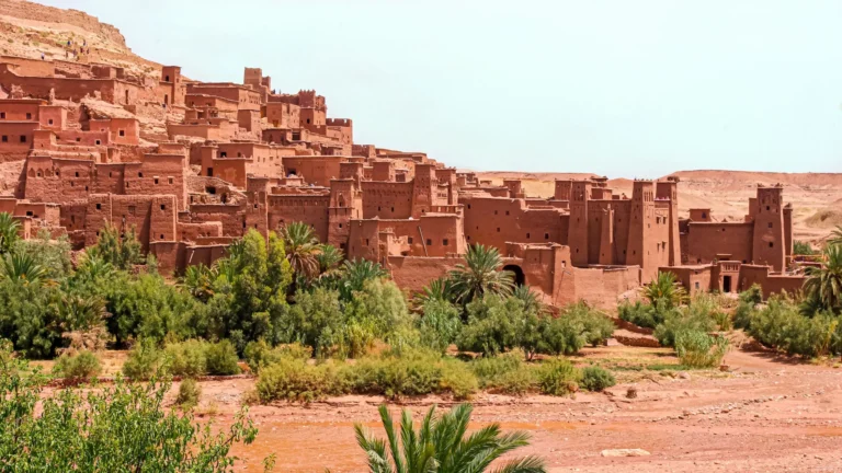 Earthen walls and towers of Aït Benhaddou above a dry riverbed, the first big stop on a Marrakech to Fes desert tour