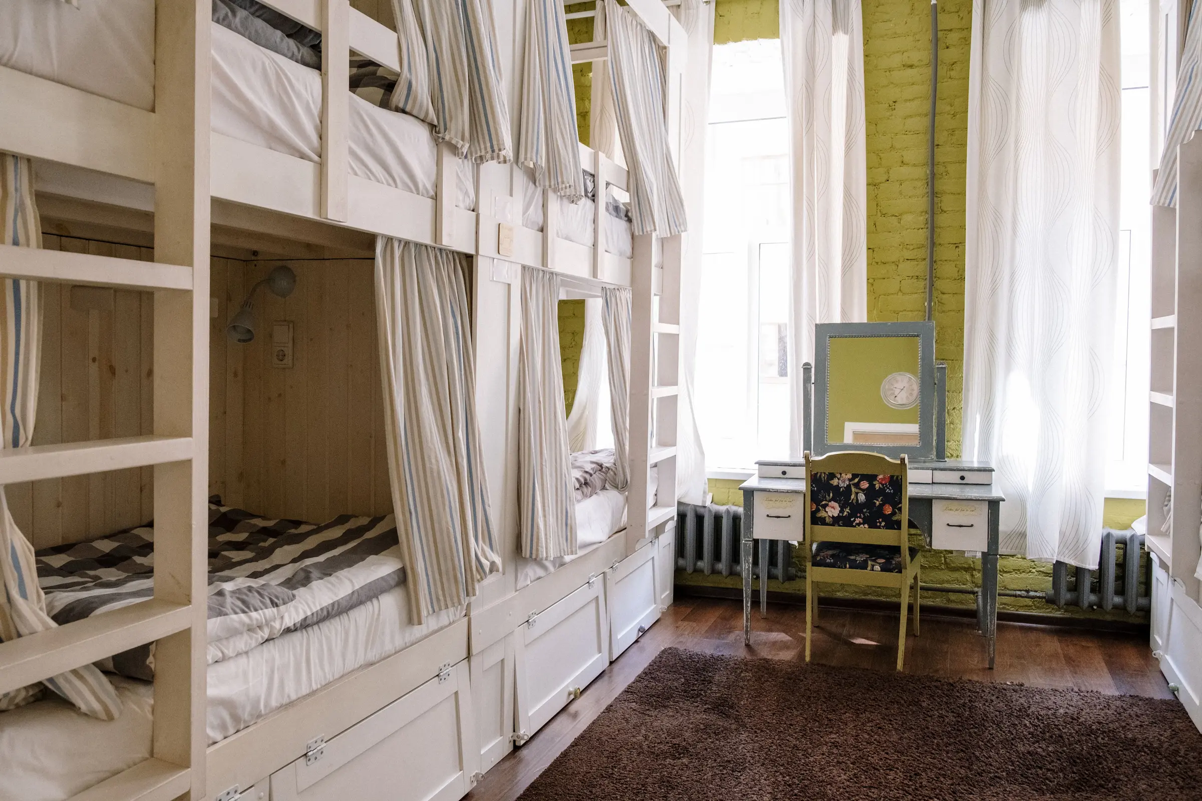 A traveler resting on a lower bunk with a curtain and eye mask in a quiet dorm